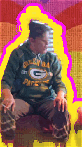 a man wearing a green bay packers hoodie is sitting on a chair