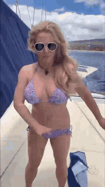 a woman in a bikini and sunglasses is standing on a boat in the water .