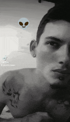 a black and white photo of a shirtless man with a tattoo on his chest and a tiktok icon in the background