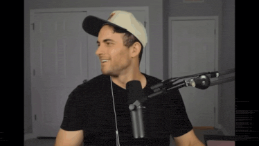 a man wearing a hat and headphones stands in front of a black microphone