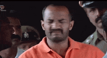 a man in an orange shirt is making a funny face in front of a crowd of people .