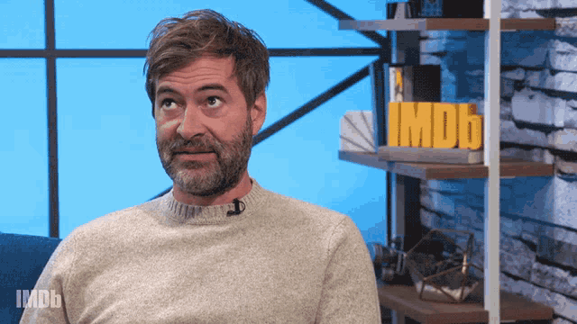a man with a beard is sitting in front of a sign that says imdb