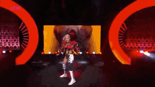 a female wrestler is walking on a stage in front of a large red screen .