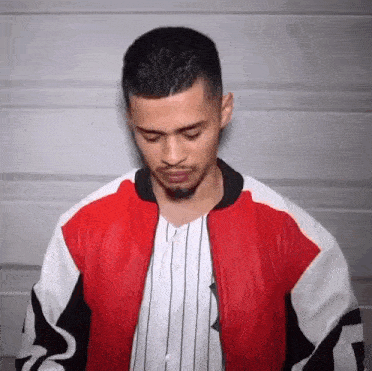 a man is wearing a red , white and black jacket and a baseball jersey .