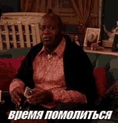 a man in a pink shirt is sitting on a couch holding a glass and a dollar bill