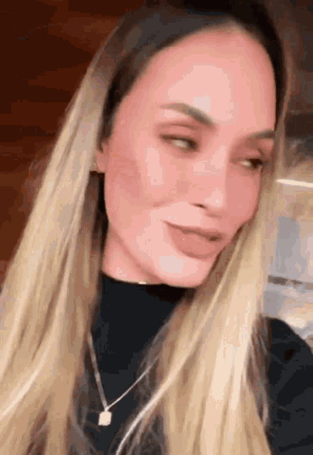 a close up of a woman 's face with long blonde hair and a necklace .