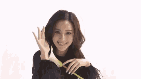 a woman in a black sweater is holding a flower in her hand and smiling .