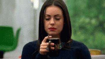 a woman is drinking a cup of coffee while sitting at a table .