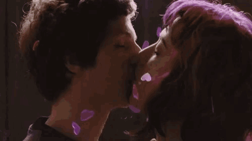 a man and a woman are kissing in front of a purple background .