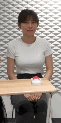 a woman in a white shirt is sitting at a desk with a red button on it .