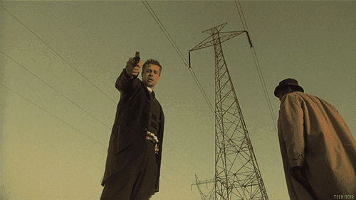 a man pointing a gun at another man in front of a telephone pole that says techdir