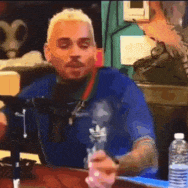 a man is sitting at a table with a bong in his hand and a bottle of water next to him .
