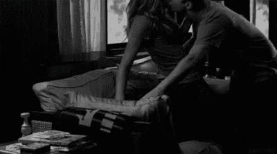 a man and a woman are kissing on a couch in a black and white photo .