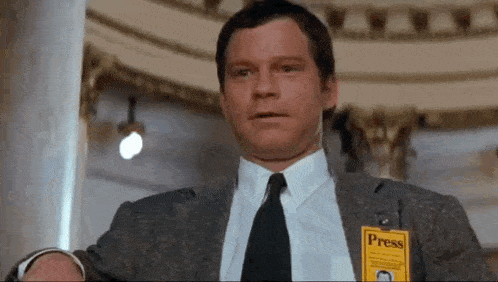 a man in a suit and tie is wearing a press badge on his chest .