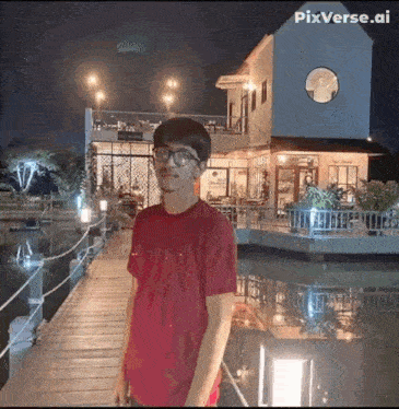 a man in a red shirt and glasses is standing on a pier in front of a building .