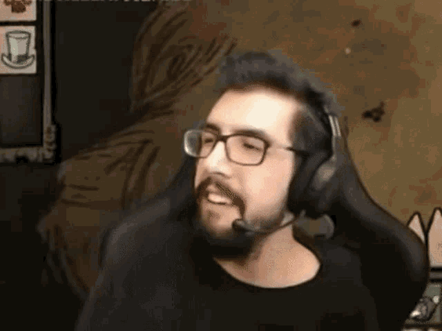 a man with a beard and glasses is wearing headphones and a microphone while playing a video game .