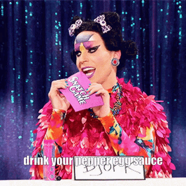a drag queen holding a card that says sweet game drink your pepper egg sauce