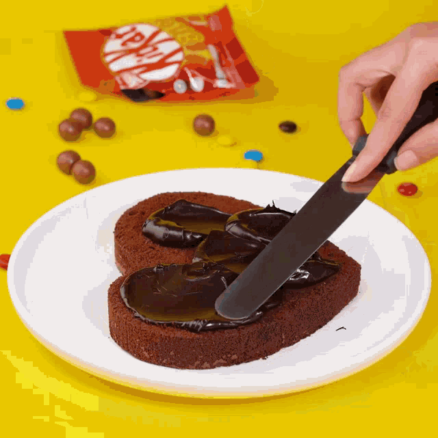 a person is spreading chocolate on a heart shaped cake on a white plate