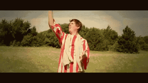 a man in a red and white striped shirt is standing in a field with his arms in the air
