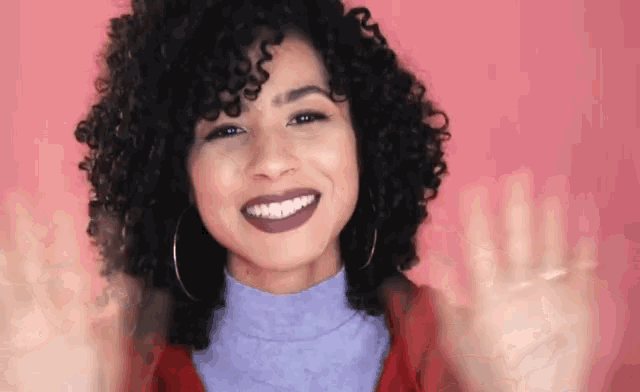 a woman with curly hair is smiling and waving her hand .