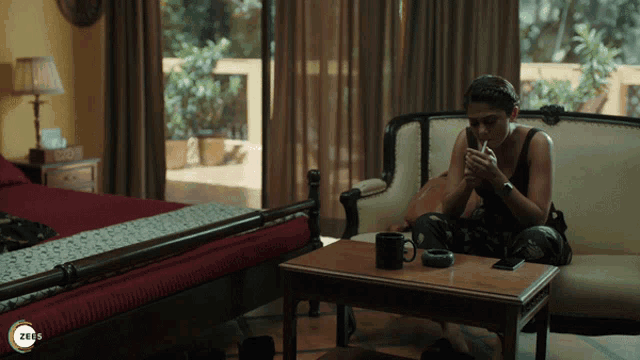 a woman sits on a couch smoking a cigarette in a room with a zees logo
