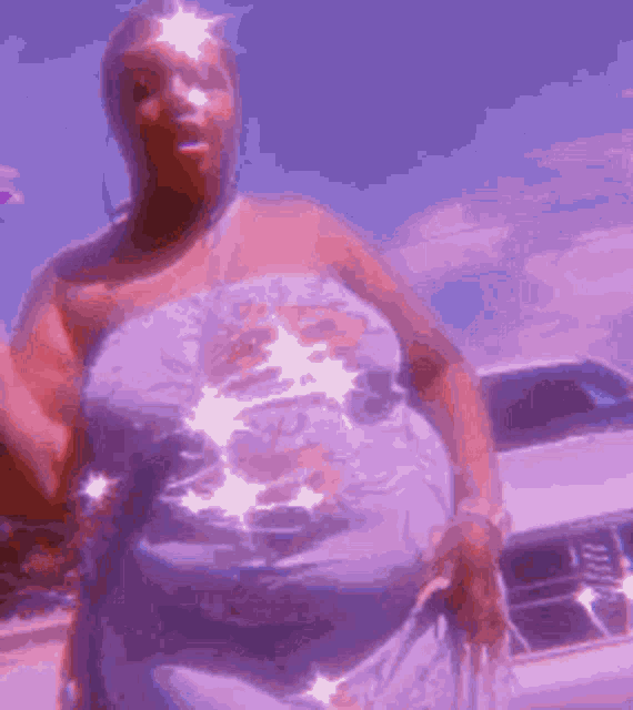 a woman in a purple dress is standing in front of a car and looking at the camera .