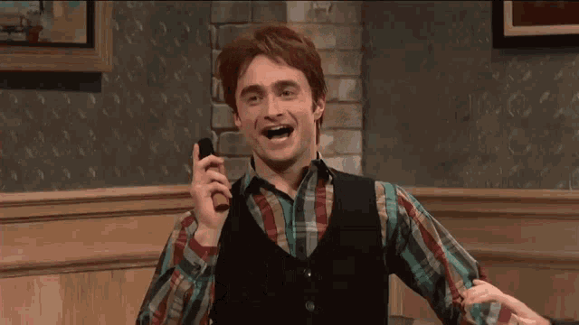 a man in a plaid shirt and vest is smiling while talking on a cell phone