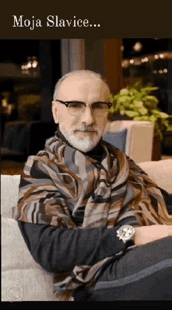 a man with glasses and a scarf is sitting on a couch with the words moja slavice written above him