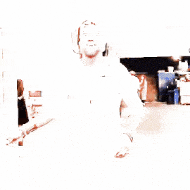 a man with a beard wearing a white shirt and a baseball cap is walking down a hallway .