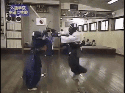a man is holding a sword in a room while another man is holding a sword .