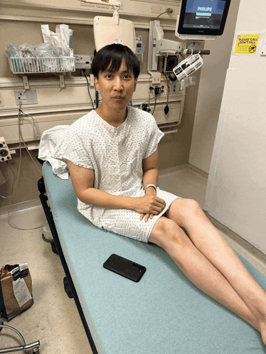a man in a hospital gown sits on a bed with a philips monitor in the background