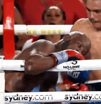 a man is sleeping in a boxing ring with a no limit boxing glove on his face .