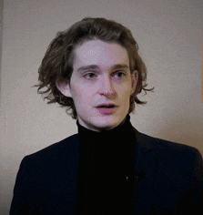 a young man with long hair is wearing a black turtleneck and a black suit .