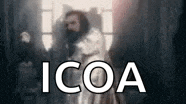 a man with a beard is standing in front of a window with the words `` icoa '' written on it .