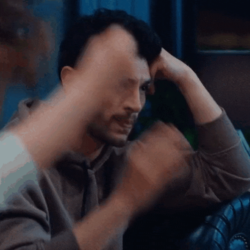 a man is sitting on a couch with his hand on his forehead .