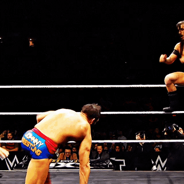 two men are wrestling in a ring and one of them is wearing shorts with the word wonder woman on them