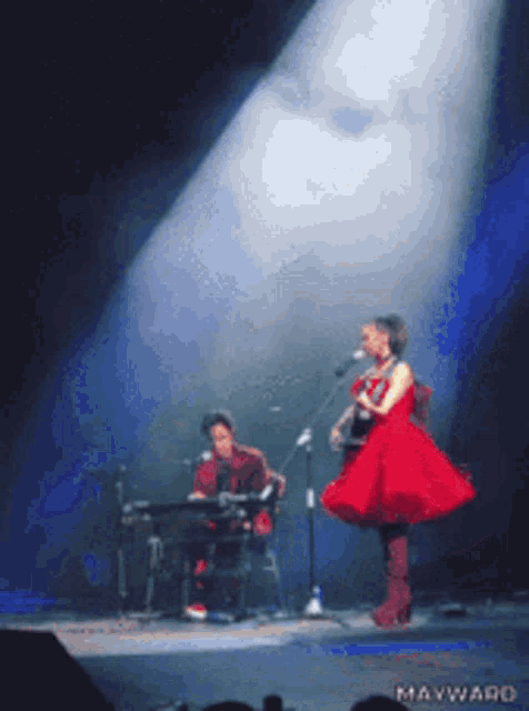 a woman in a red dress is singing into a microphone while a man plays keyboard