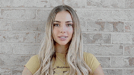 a woman in a yellow shirt is standing in front of a brick wall