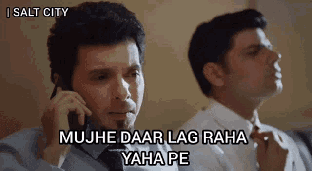 a man talking on a cell phone next to another man who is adjusting his tie .