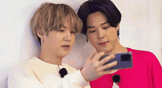 two young men are looking at a cell phone together