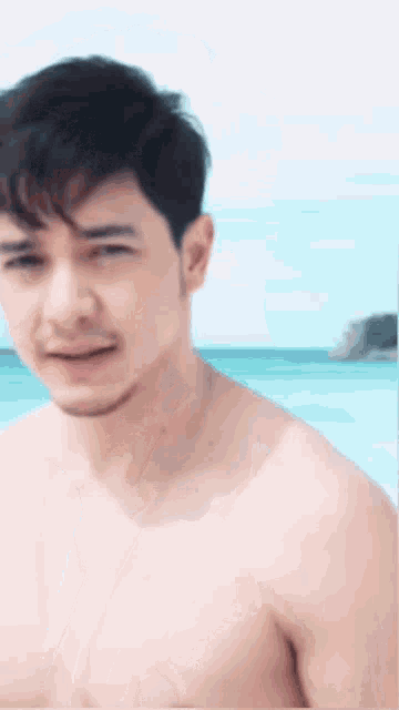 a shirtless man with a beard is standing on the beach
