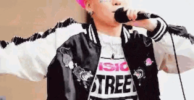 a man is singing into a microphone while wearing a pink hat and a black jacket .
