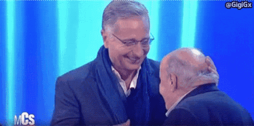 a man in a suit and scarf is laughing with another man on a stage .
