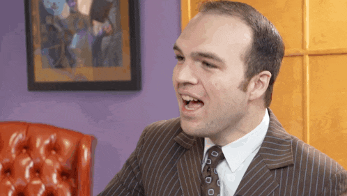 a man in a suit and tie is making a funny face in front of a purple wall