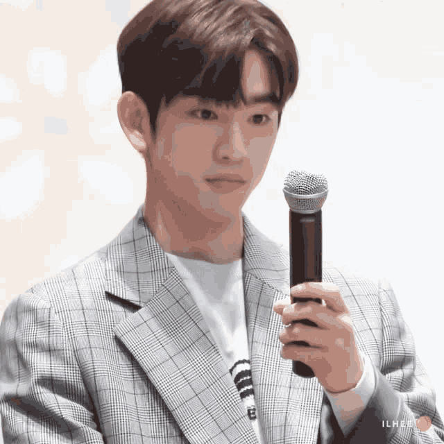 a man in a plaid jacket holds a microphone in his hand