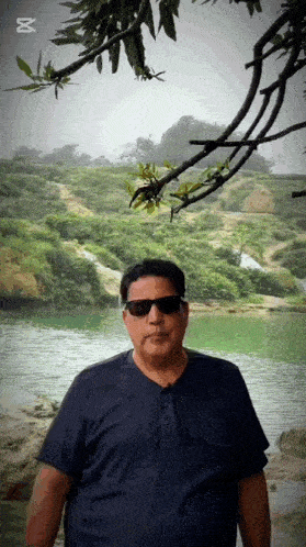 a man wearing sunglasses is standing in front of a lake