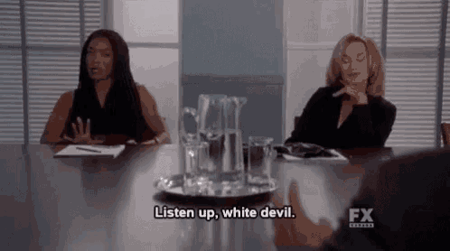 two women are sitting at a table with glasses of water and talking to each other .