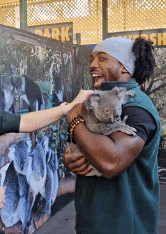 a man holding a koala bear in front of a sign that says " park "