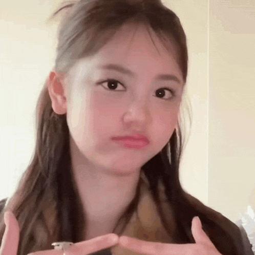 a young girl is making a funny face and making a heart with her fingers .