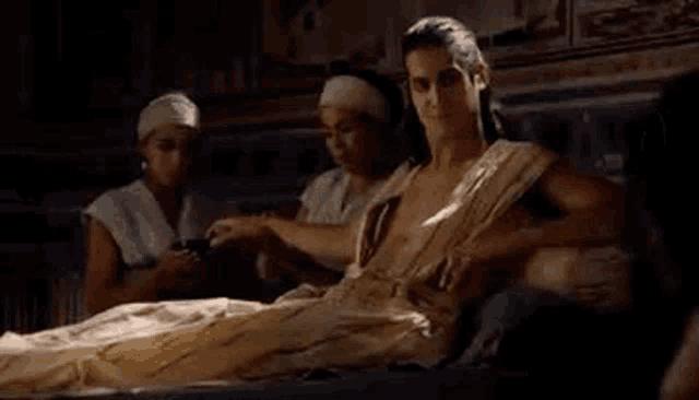 a man is laying on a bed with a group of people standing around him .